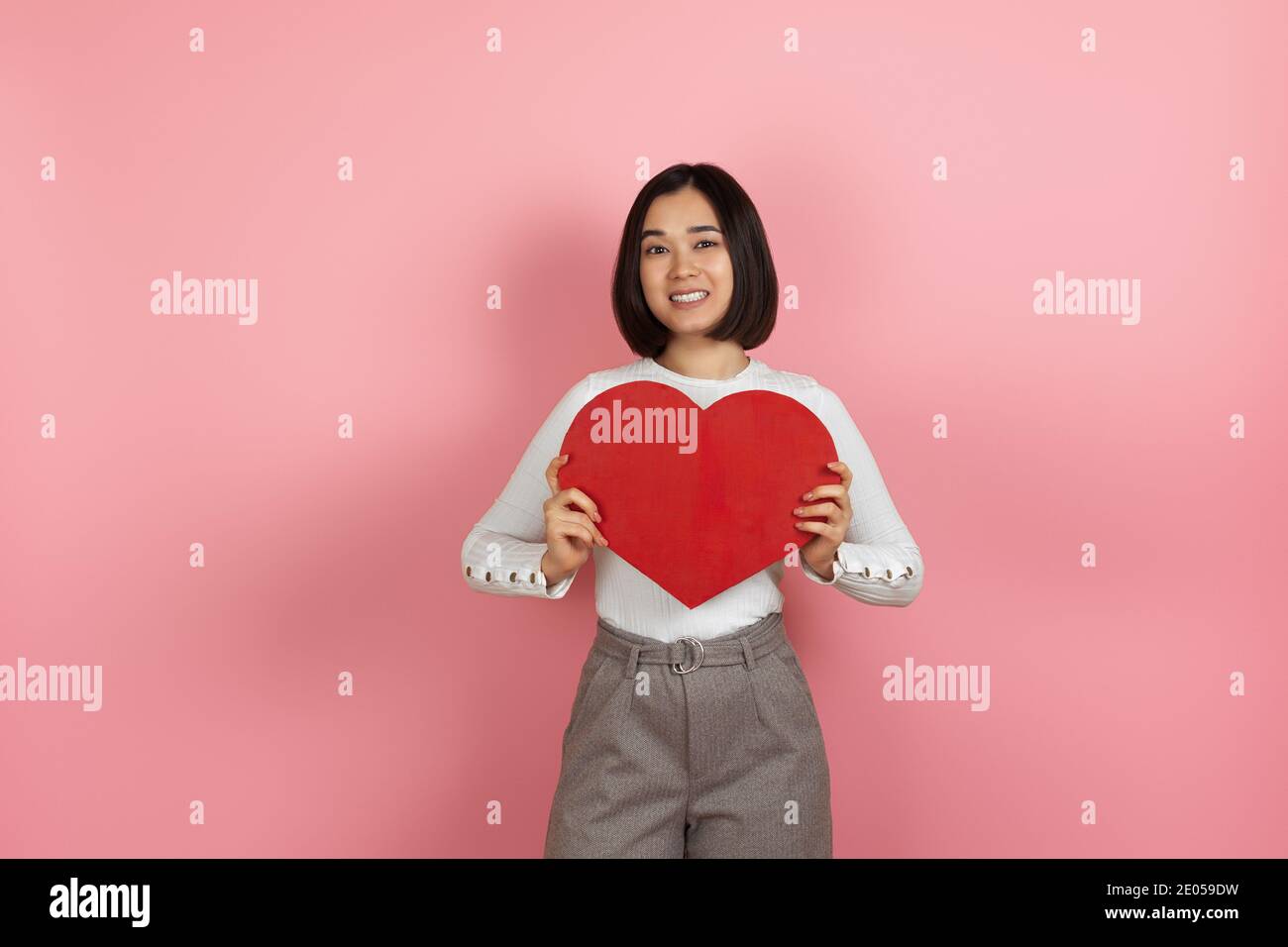 Mock up lächelnd glücklich schöne junge asiatische Frau hält groß Rotes Papier Herz als Liebeserklärung isoliert auf Rosa Hintergrund Stockfoto