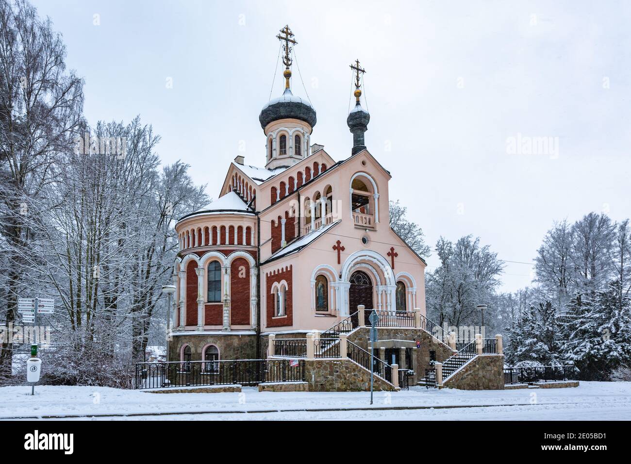 Marianske Lazne, Tschechische Republik - Dezember 29 2020: Winteransicht der orthodoxen russischen Kirche St. Wladimir mit roter Fassade, umgeben von Bäumen. Stockfoto