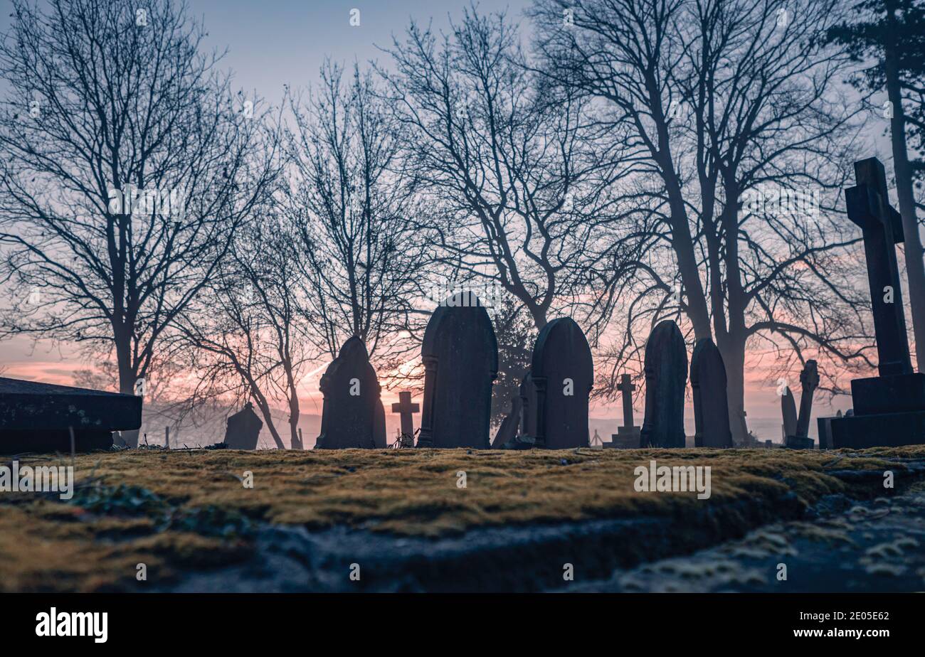 Ein feierliches Bild von Grabsteinen in einem Kirchhof an einem nebligen launischen Sonnenaufgang Morgen. Stockfoto