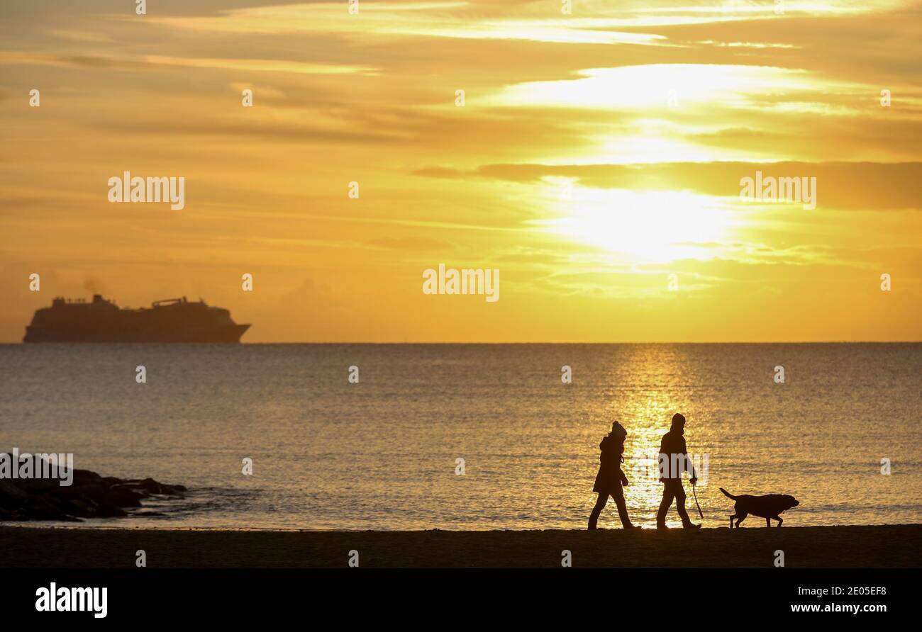 Sandbanks, Großbritannien. Dezember 2020. Hundespaziergänger bei Sonnenaufgang am Strand von Sandbanks in Poole, Dorset. Kredit: Richard Crease/Alamy Live Nachrichten Stockfoto