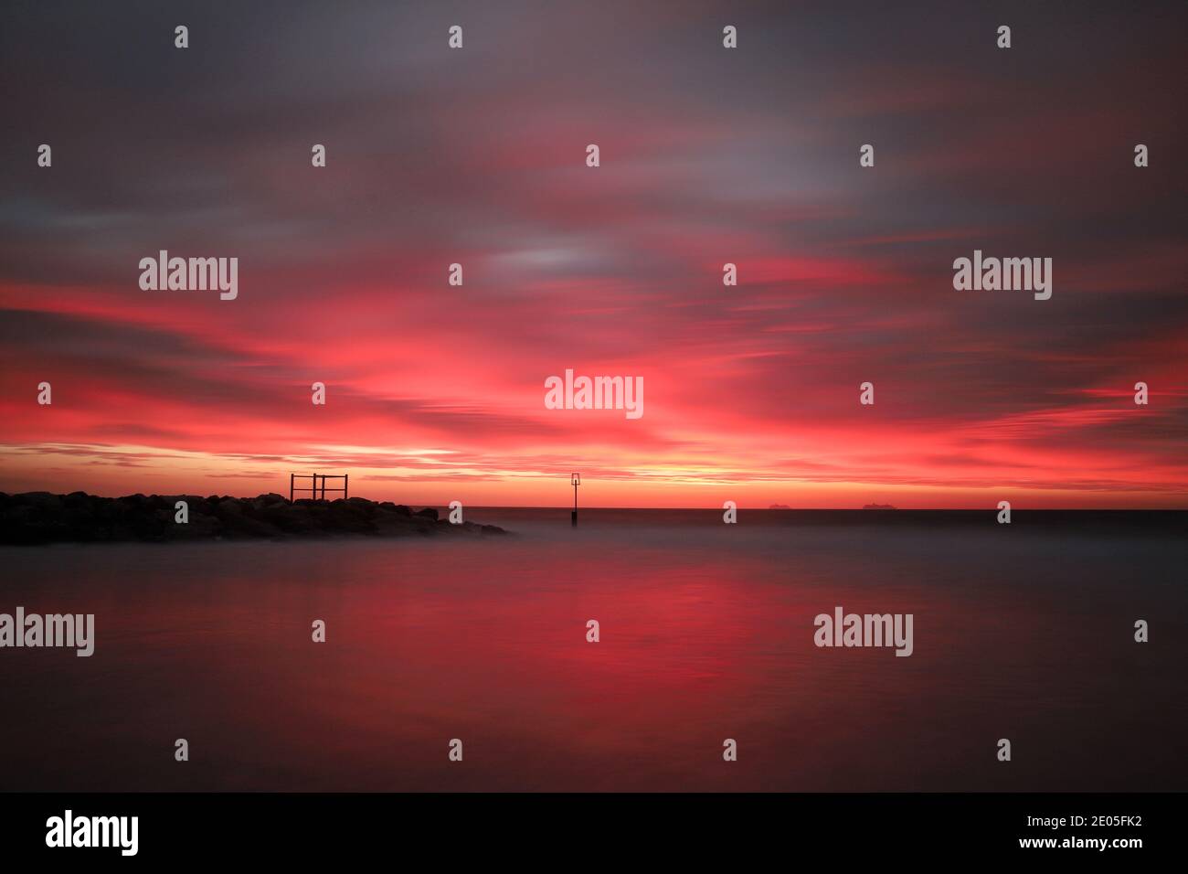 Eine lange Belichtung erfasst Streifen von leuchtendem Karmesin in einem Himmel, der mit dicken, dunklen Regenwolken über Bournemouth Beach übersät ist. Stockfoto