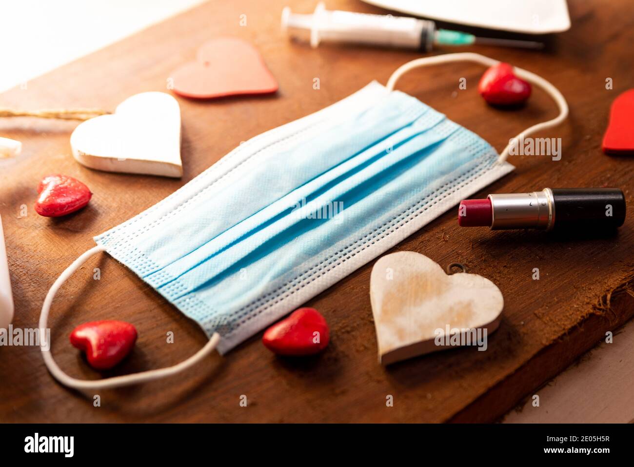 Covid valentinstag Hygiene-Konzept. Gesichtsmaske mit roten Herzen auf Holz Hintergrund. Draufsicht der Hand Desinfektionsmittel und Lippenstift und Spritze für den Urlaub Stockfoto