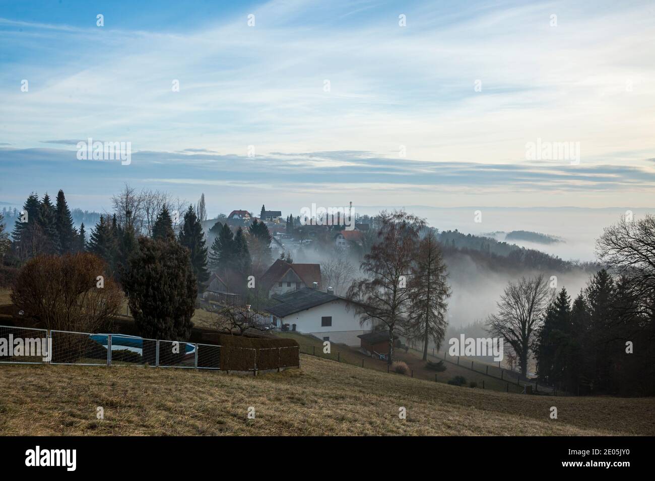 Malerische Drohne Blick auf grünes Tal mit kleinem Dorf von Bäumen umgeben in der Nähe der Bergkette der Alpen in nebligen Morgen. Stockfoto