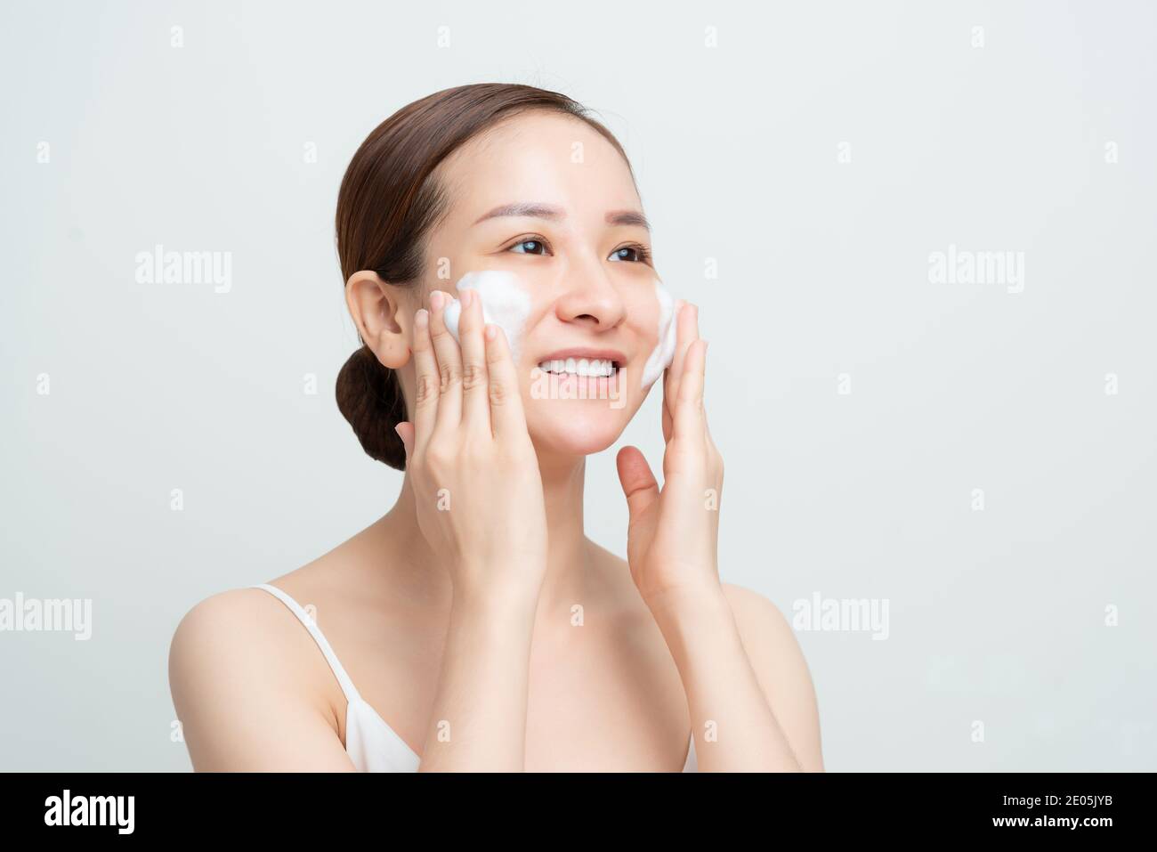 Nahaufnahme von glücklich lächelnden asiatischen Frau mit täglichen Pflege Hautreinigungsschaum und schauen erfreut, weißen Hintergrund Stockfoto