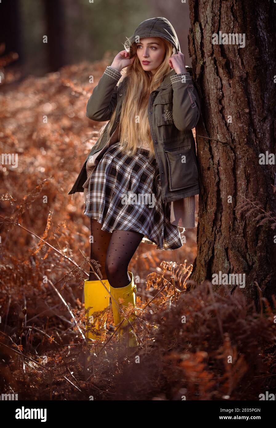 Junge natürlich schöne Frauen in einem Wald mit orange herbstlichen Winterfarben tragen einen grünen Mantel mit der Kapuze in einem redaktionellen Mode-Set. Stockfoto