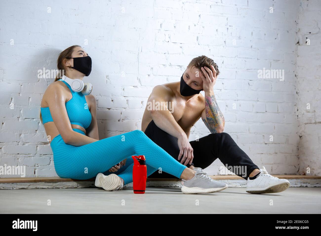 Ruhe. Professionelle Athleten Training auf Backstein Wand Hintergrund tragen Gesichtsmasken. Sport während Quarantäne von Coronavirus weltweit Pandemie. Junges Paar üben im Fitnessraum sicher mit Geräten. Stockfoto