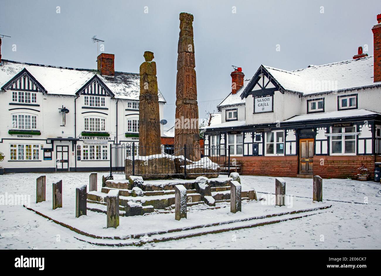 Alte sächsische Steinkreuze im gepflasterten schneebedeckten Markt Platz im Winter bei Sandbach Cheshire vor dem Markt Wirtshaus und sächsischer Grill Stockfoto