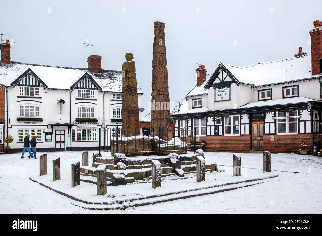 Alte sächsische Steinkreuze im gepflasterten schneebedeckten Markt Platz im Winter bei Sandbach Cheshire vor dem Markt Wirtshaus und sächsischer Grill Stockfoto
