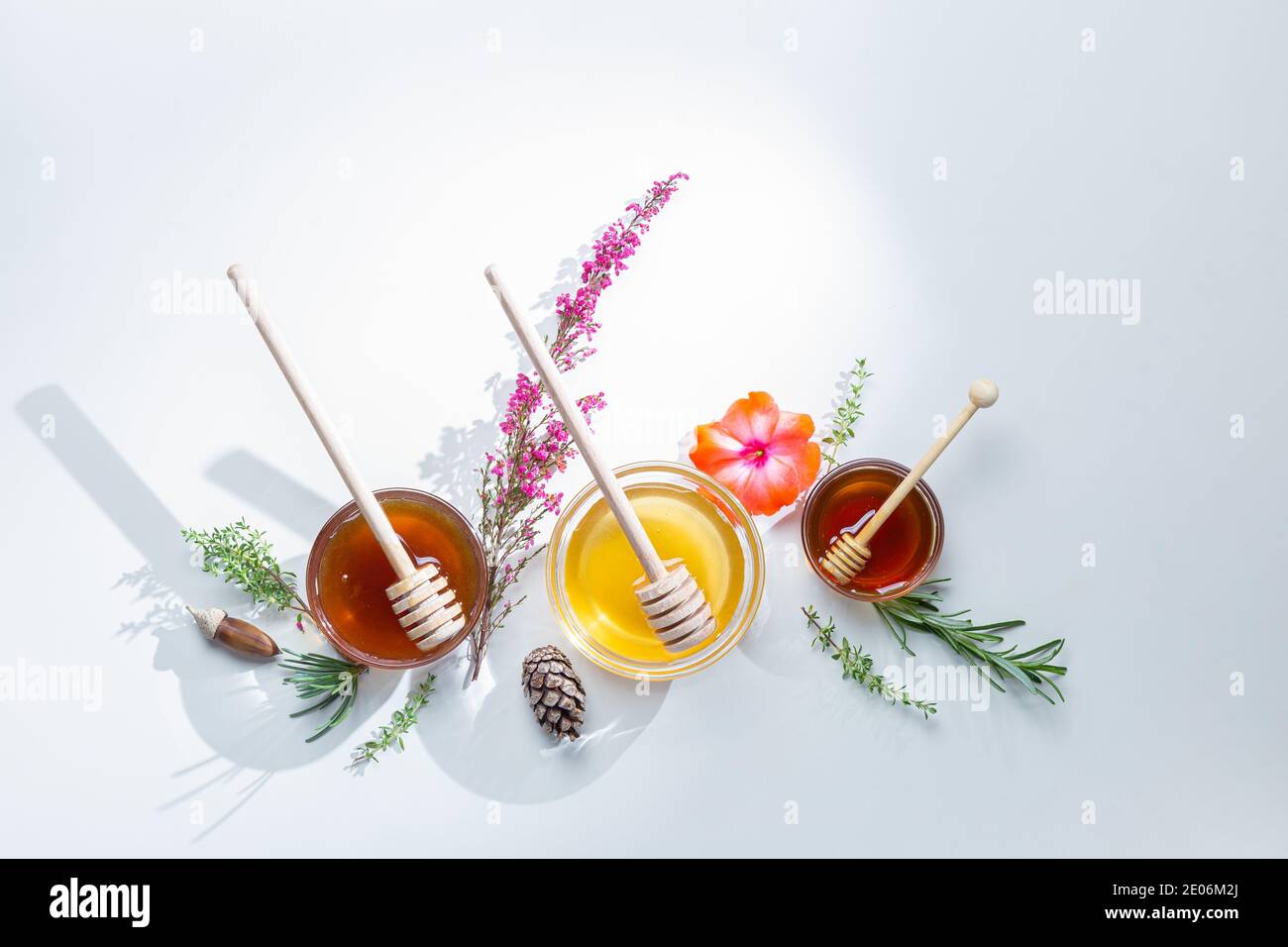 Zusammensetzung von Honiggläsern mit Honigstäbchen und Blumen, auf weißem Hintergrund. Stockfoto