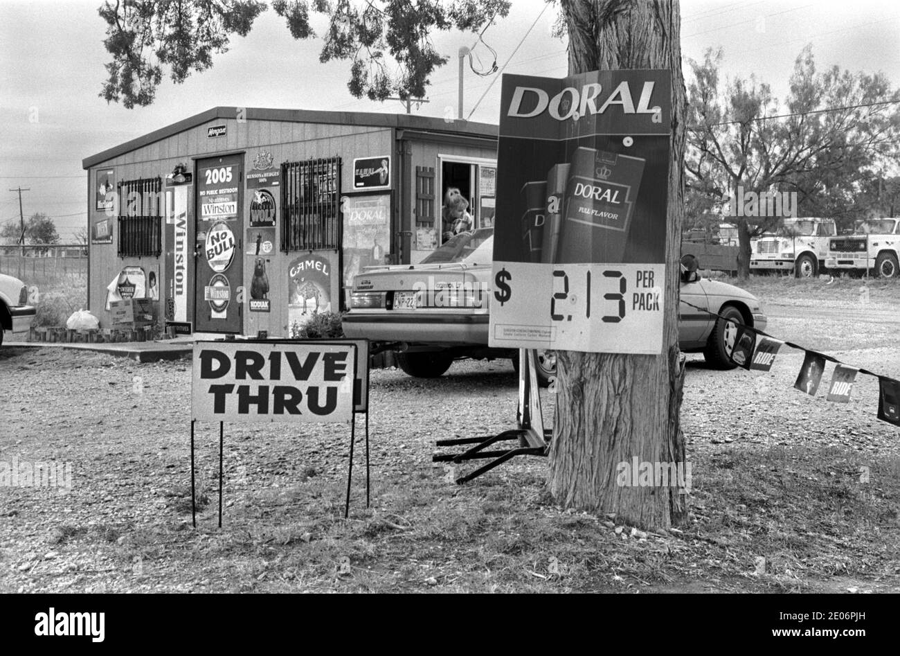 Drive Thru Drive im Fast Food Restaurant 1990s USA. Frau, die sich hinlehnt und einen Kunden in seinem Auto bedient. Sweetwater, Texas 1999 USA. Die Fahrt durch das Gebäude des Fast-Food-Restaurants, das mit Zigarettenverkäufen und Werbetafeln VON HOMER SYKES bedeckt ist Stockfoto