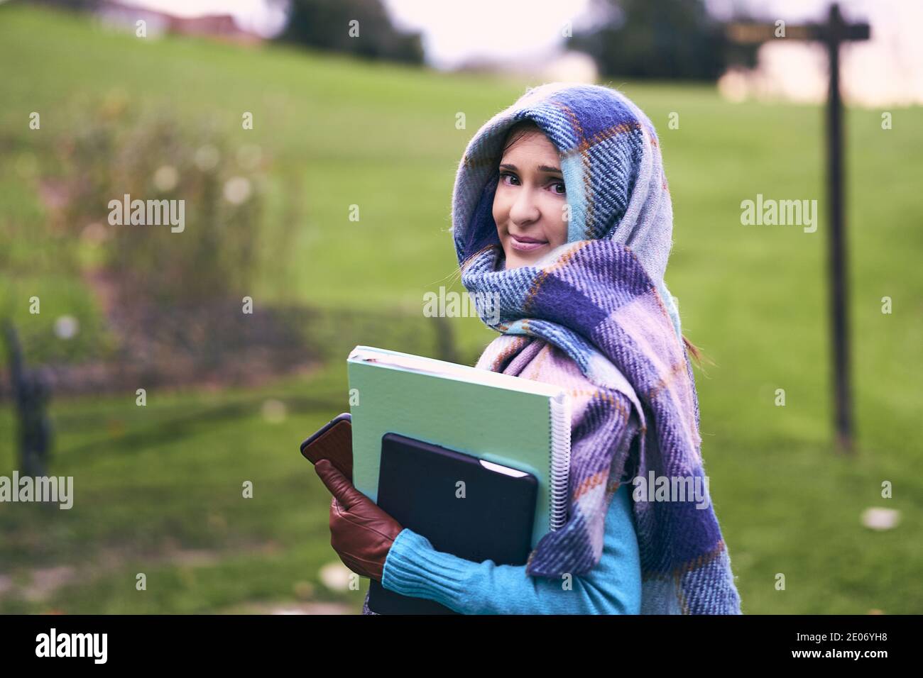 Schöne Studentin mittleren Alters zu Fuß im Park mit Notebook und Tablet trägt ihren Sohn. Mutterschaft und Studium Konzept. Erwachsenenalter Studien Stockfoto