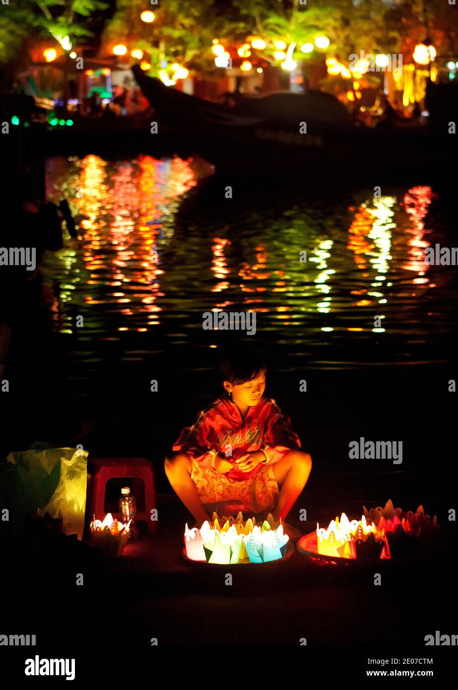 Mädchen verkaufen Papierlaternen auf dem Vollmond-Festival in Hoi an, Vietnam mit Lichtern im Fluss reflektiert Stockfoto