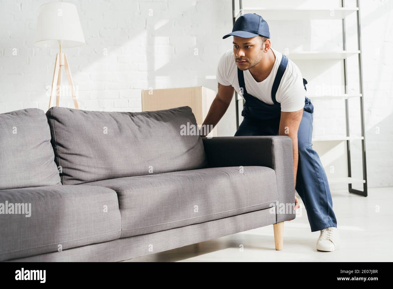 Indian Mover in Uniform und Mütze tragen Sofa in der Wohnung Stockfoto