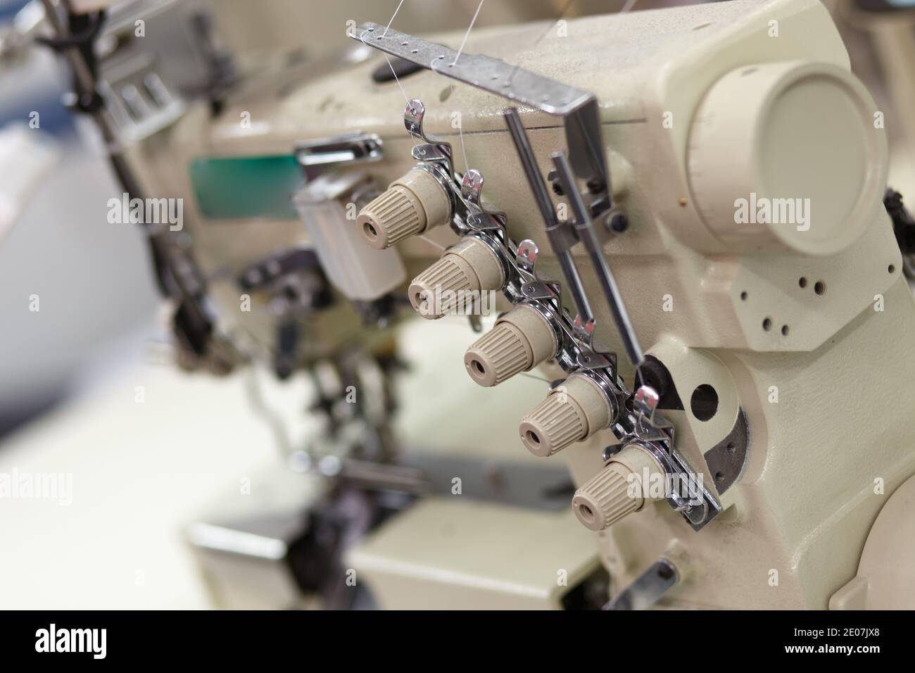 Professionelle Nähmaschine mit Faden in der Werkstatt. Ausrüstung zum Einkanten, Säumen oder Verschließen von Kleidung in Schneiderei. Stockfoto