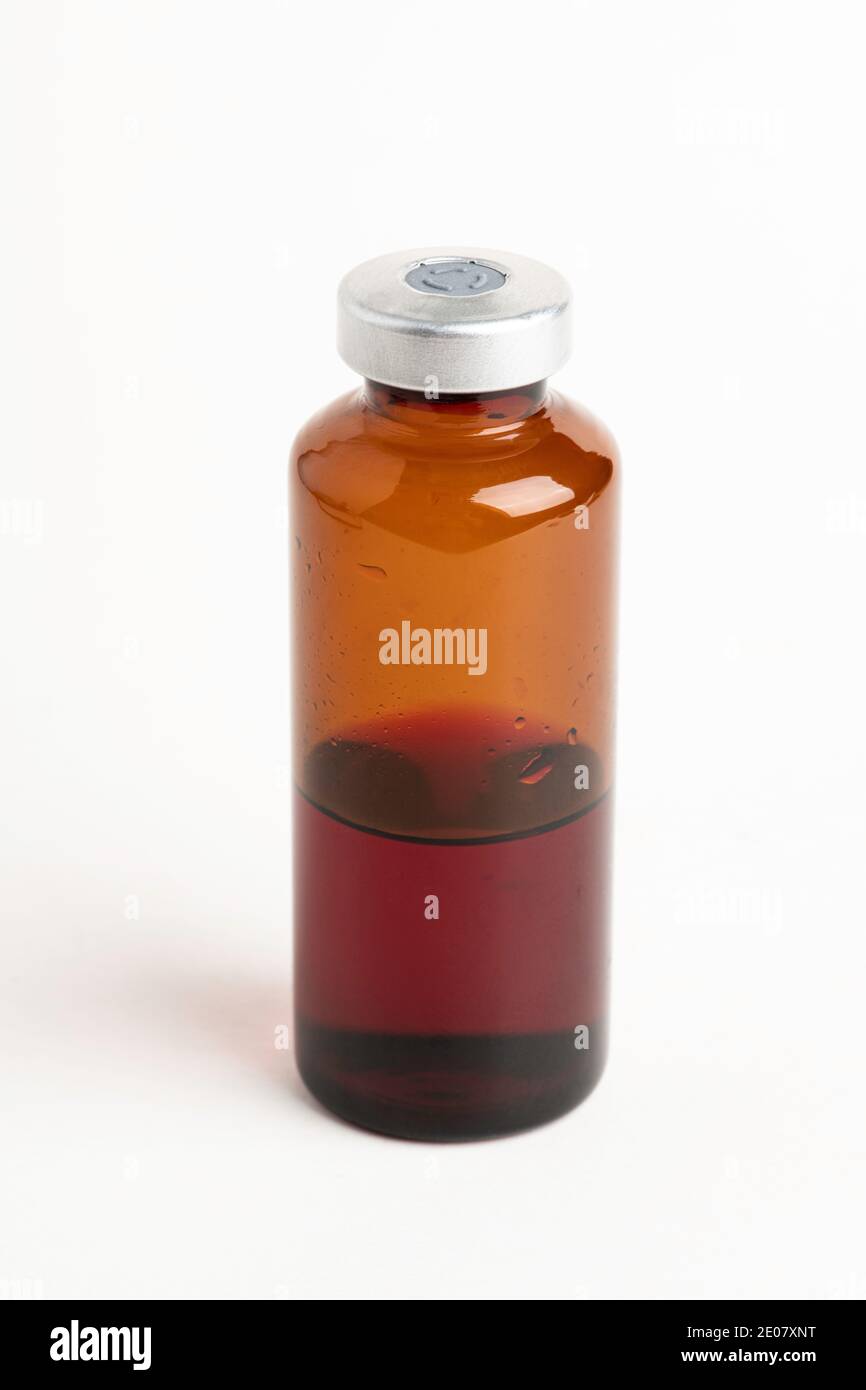 Eine Makroaufnahme mit selektivem Fokus einer bernsteinfarbenen Impfstoffflasche auf einem schlichten weißen Hintergrund. Stockfoto