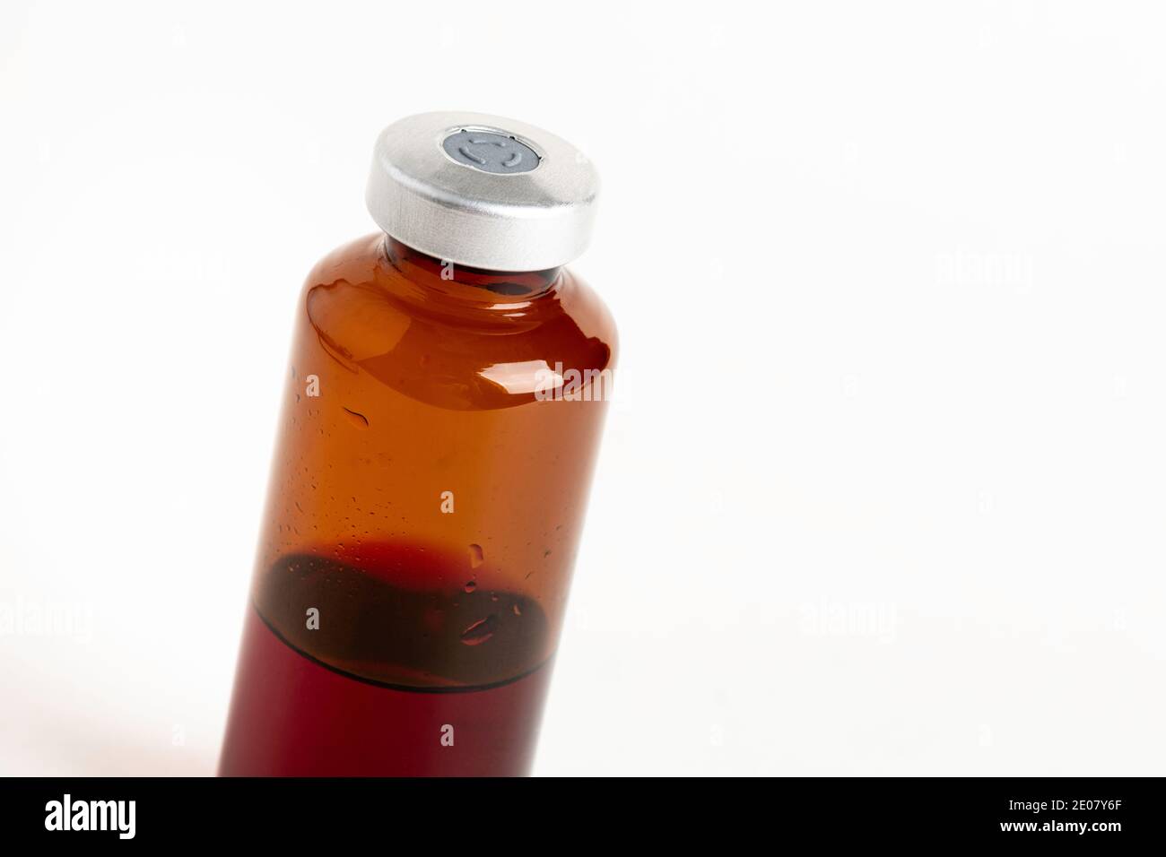 Eine Makroaufnahme mit selektivem Fokus einer bernsteinfarbenen Impfstoffflasche auf einem schlichten weißen Hintergrund. Stockfoto