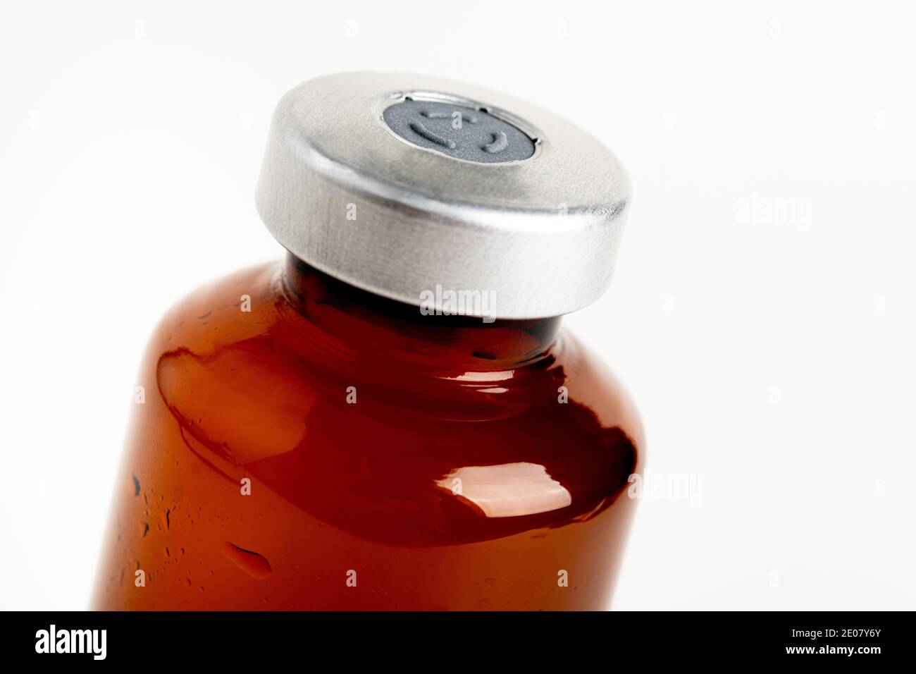 Eine Makroaufnahme mit selektivem Fokus einer bernsteinfarbenen Impfstoffflasche auf einem schlichten weißen Hintergrund. Stockfoto
