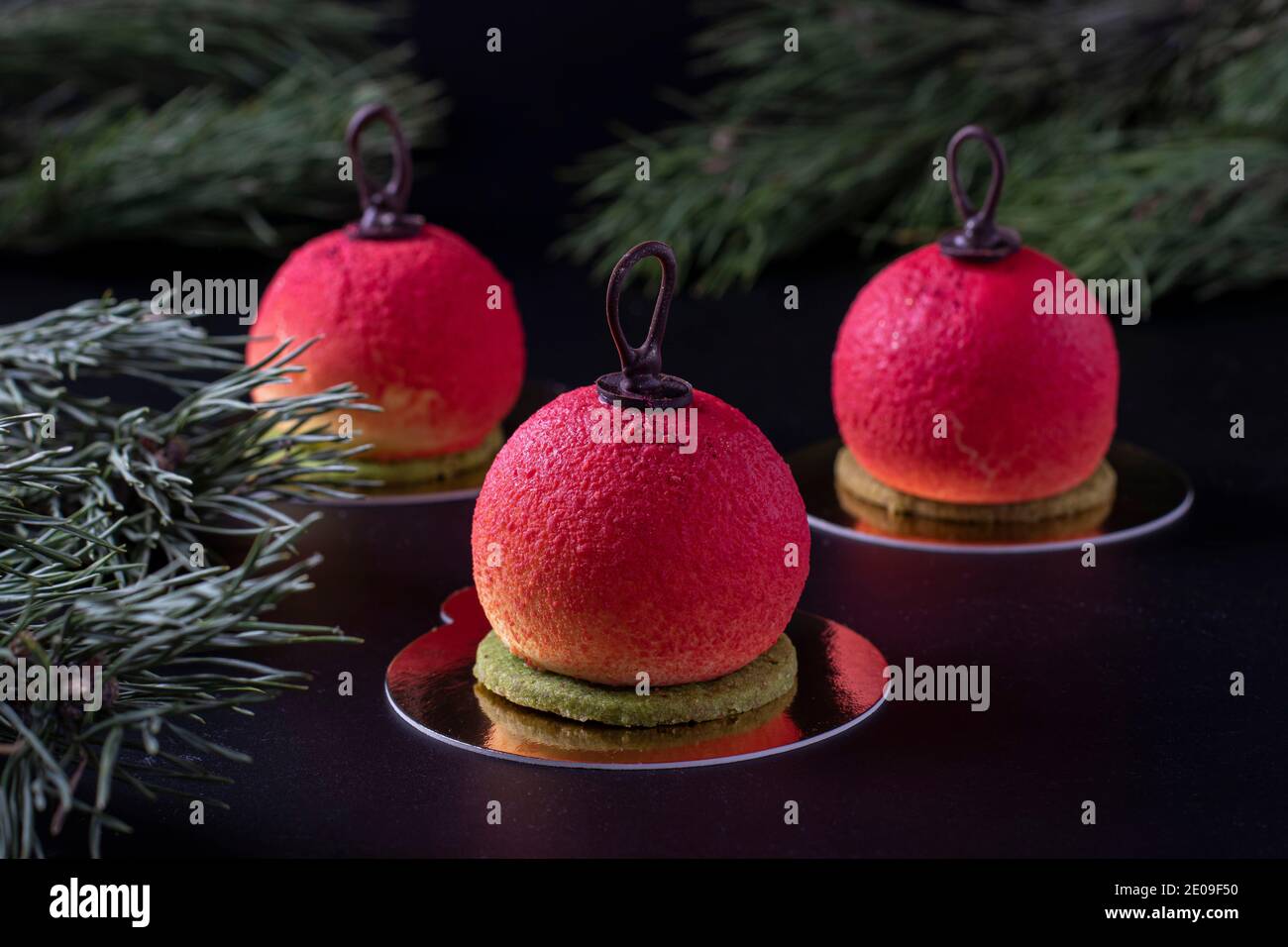 Drei Mousse Desserts in Form von Weihnachtskugeln auf dunklem Hintergrund. Silvesterparty. Stockfoto