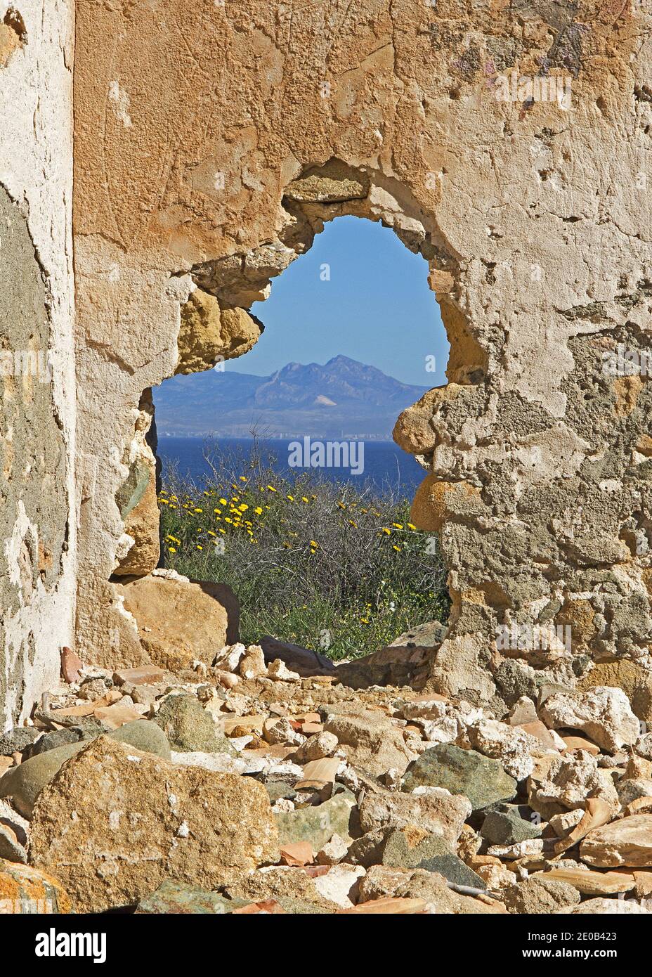 Blick durch ein Loch in der Wand einer Ruine auf der Insel Tabarca. Ein Teil der Insel hat ein wildes Aussehen mit nur wenigen Ruinen und einem Leuchtturm Stockfoto