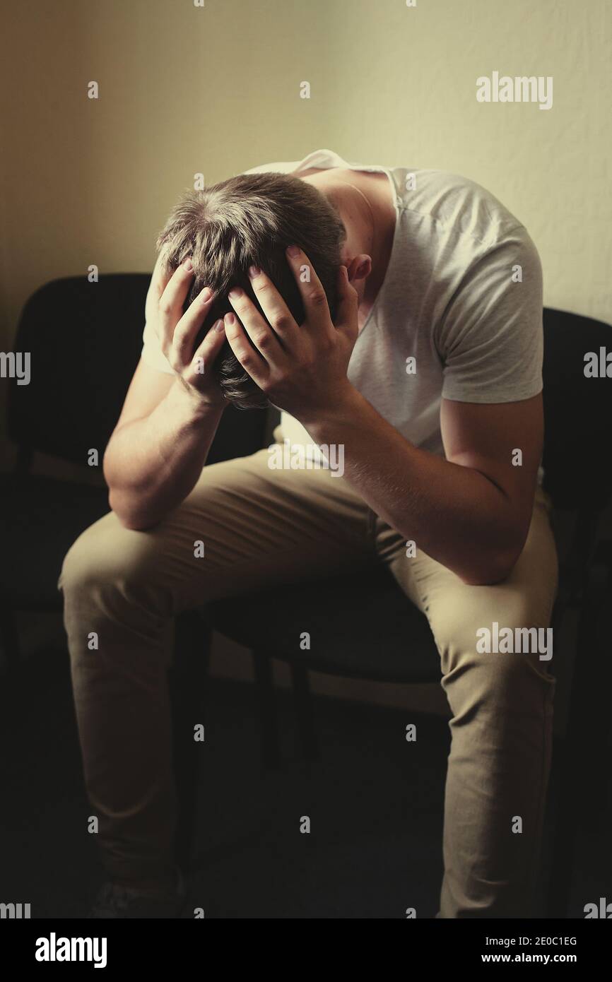 Männerprobleme. Ein junger Mann sitzt auf einem Stuhl und hält seinen Kopf in den Händen. Stockfoto