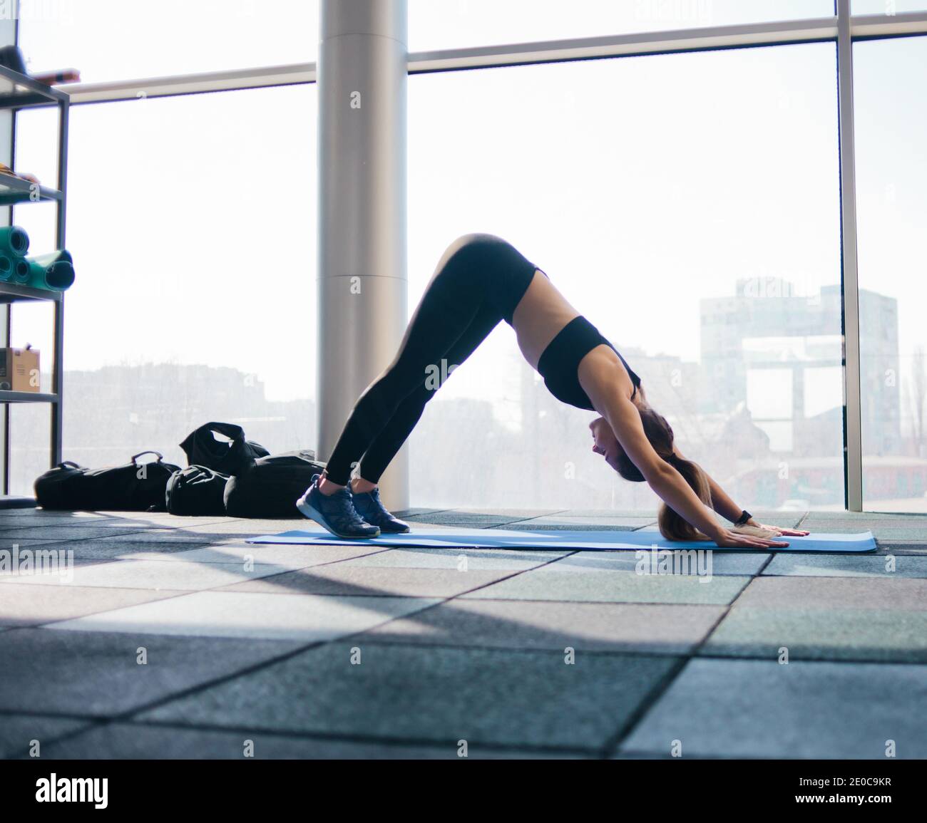 Junge Frau macht Yoga Stretching für den ganzen Körper auf Matte auf dem Hintergrund der großen Panoramafenster in der Turnhalle. Yoga-Training Stockfoto