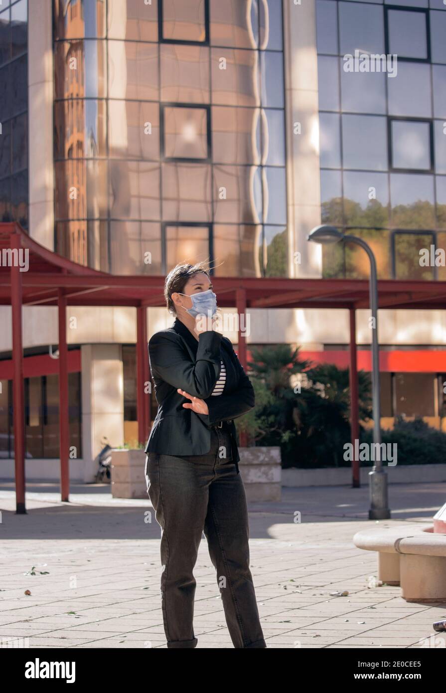 Elegante Geschäftsfrau mit Maske, die außerhalb des Büros steht, stellt sich für die Kamera im Freien. Girl Boss Konzept 2021. Stockfoto