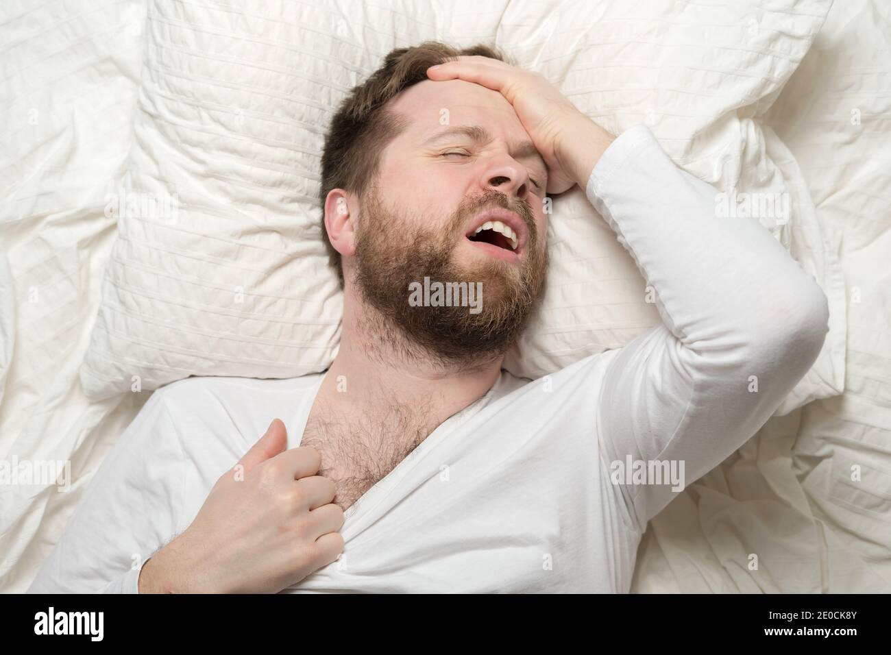 Schlaflosigkeit. Der junge Mann kann nicht schlafen, er ist stickig und hat Kopfschmerzen. Konzept der psychischen Gesundheit. Stockfoto