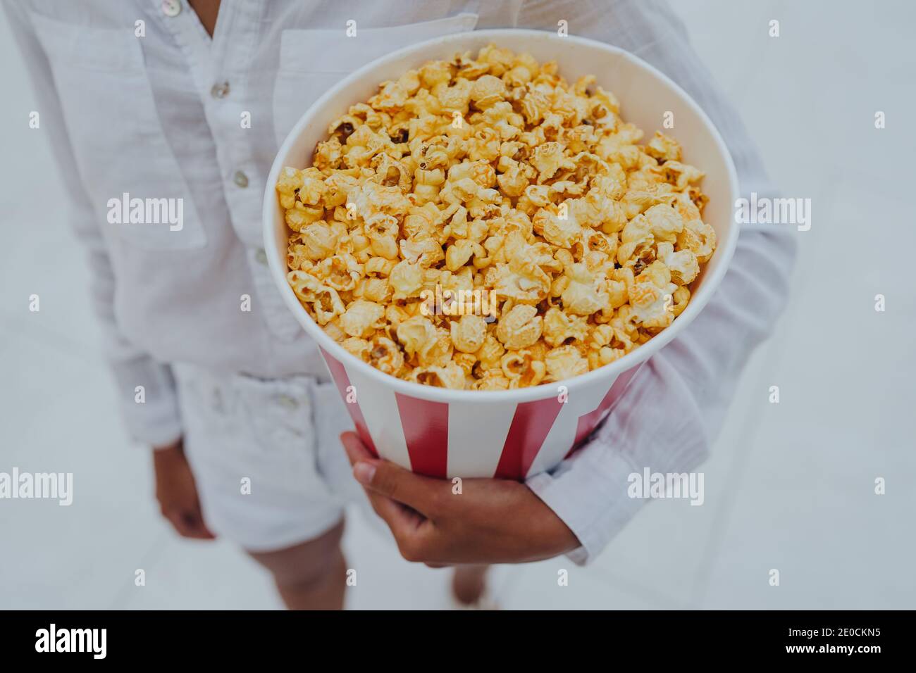 Nahaufnahme eines jungen süßen Mädchens, das eine Tube Popcorn in den Händen hält. Stockfoto