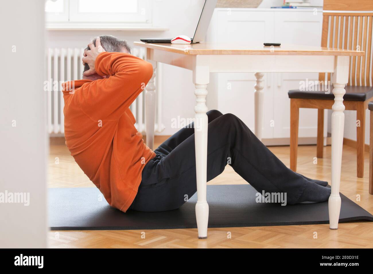 Reifer Mann tut Sit-ups zu Hause unter einem Esstisch Mit Laptop und Smartphone - konzentrieren Sie sich auf den Mann Stockfoto