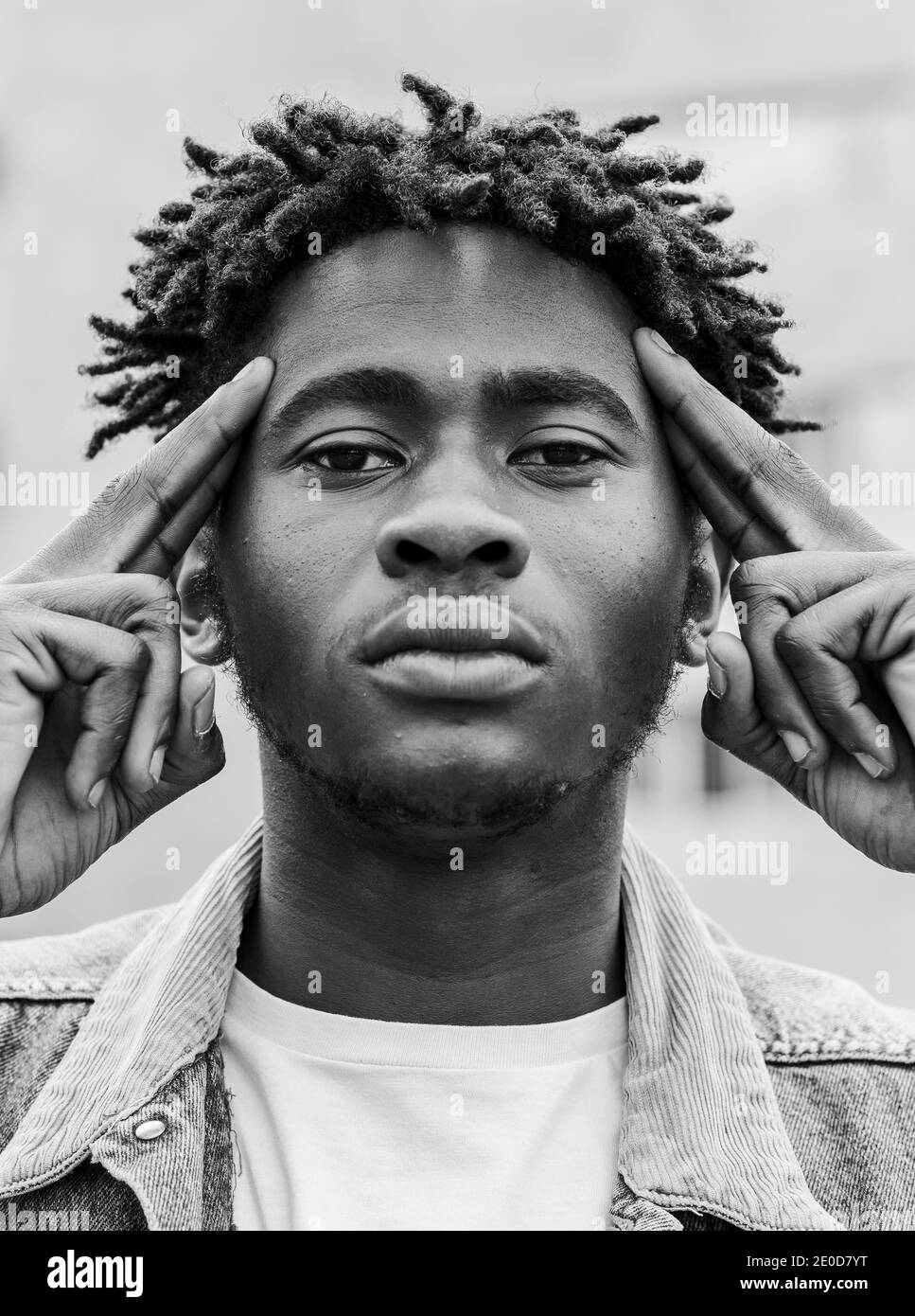 Schwarz und weiß von ernsten jungen afroamerikanischen Hipster männlich Mit Afro Frisur berühren Tempel und Blick auf die Kamera Stockfoto