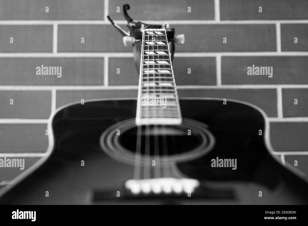 Akustische Gitarre Nahaufnahme über Backsteinwand Hintergrund. Konzentrieren Sie sich auf Klangloch und Saiten. Schwarzweiß-Fotografie Stockfoto