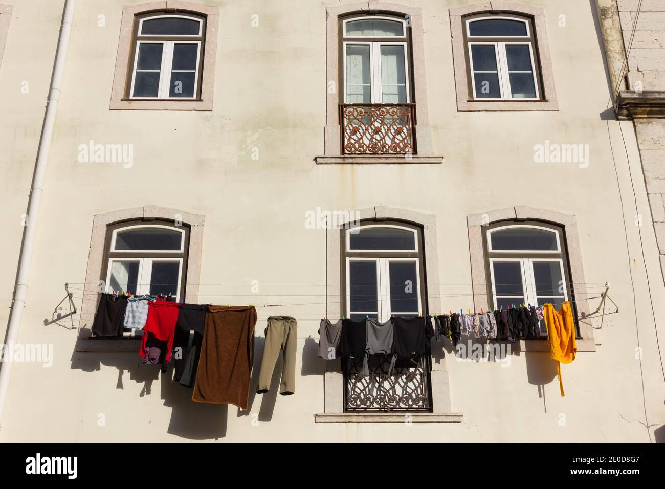 Bunte Kleidung hängt an der Fassade eines Wohngebäudes an sonnigen Tagen. Altmodische Kleidung Trocknung Stil in Lissabon, Portugal Stockfoto