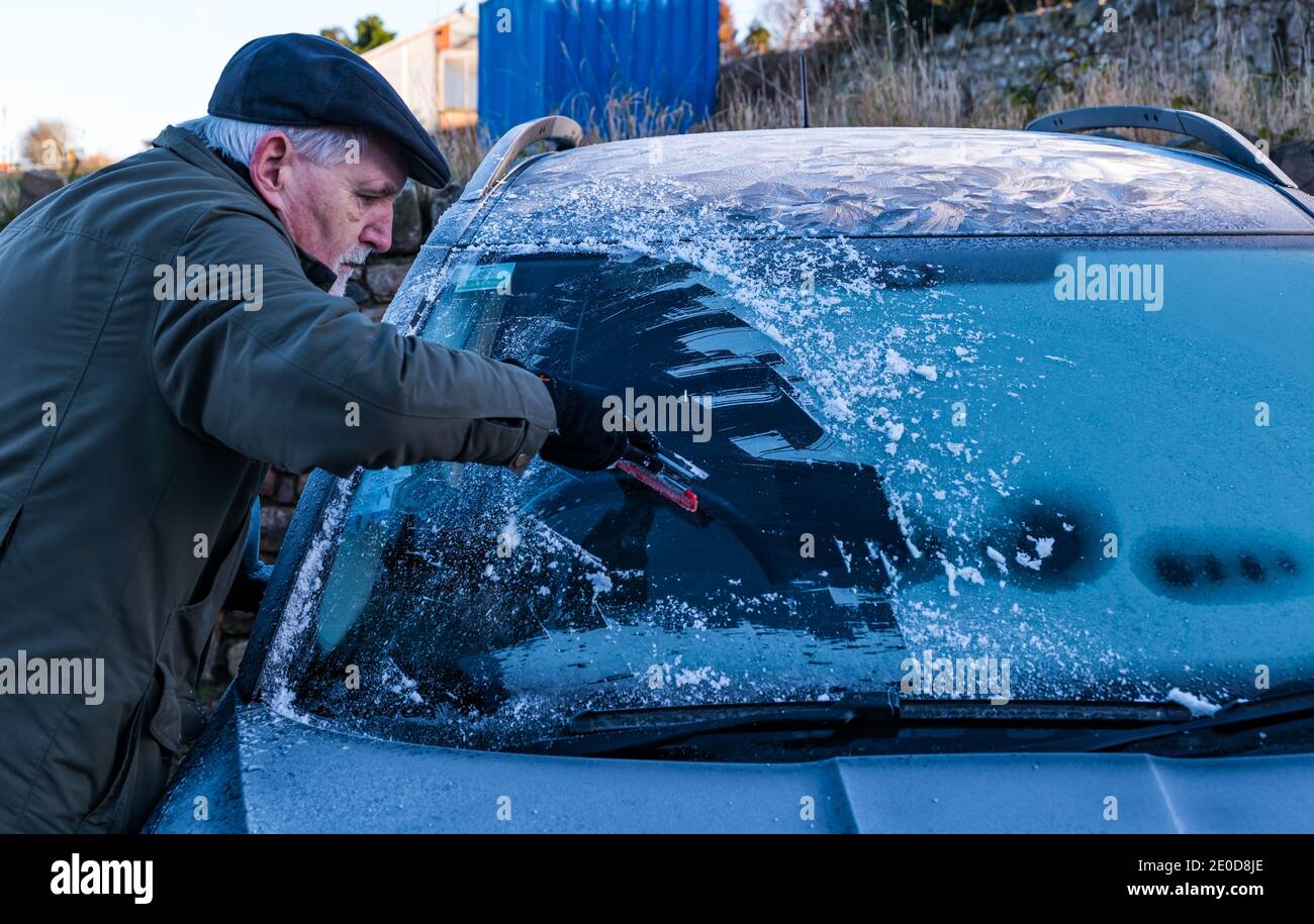 Senior man kratzt Eis von der Windschutzscheibe im Winter mit Frostmustern auf dem Autodach, Schottland, Großbritannien Stockfoto