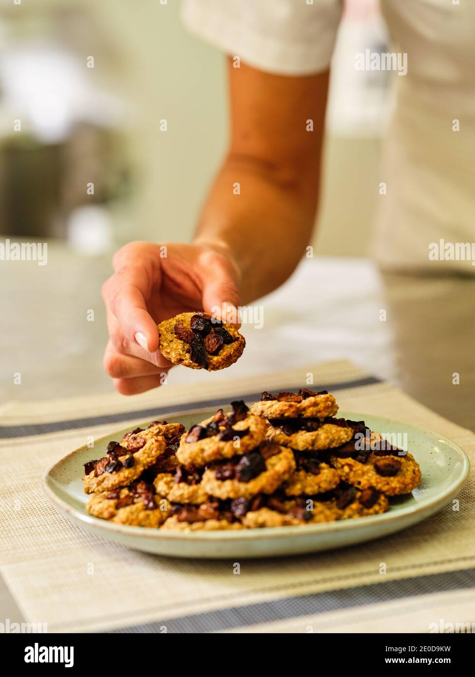 Crop anonyme Konditor setzen frisch gebackene Mürbeteig Cookies mit Getrocknete Früchte auf dem Teller während der Arbeit in der Küche Stockfoto