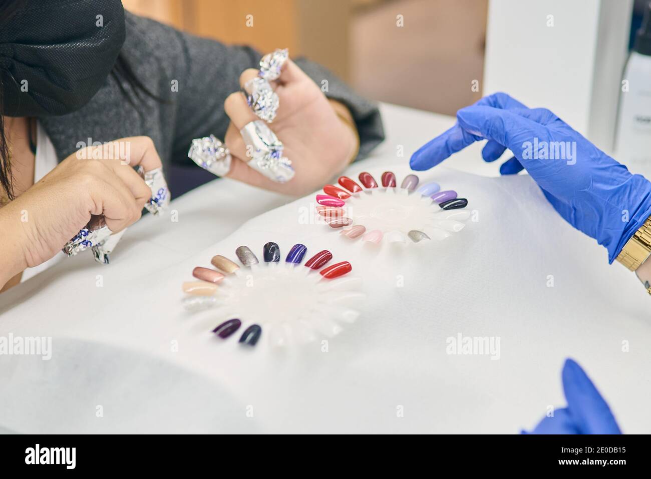 Crop anonyme Frau Wahl Farbe aus Nagellack-Palette, während am Tisch mit Meister der Maniküre in modernen Schönheitssalon sitzen Stockfoto