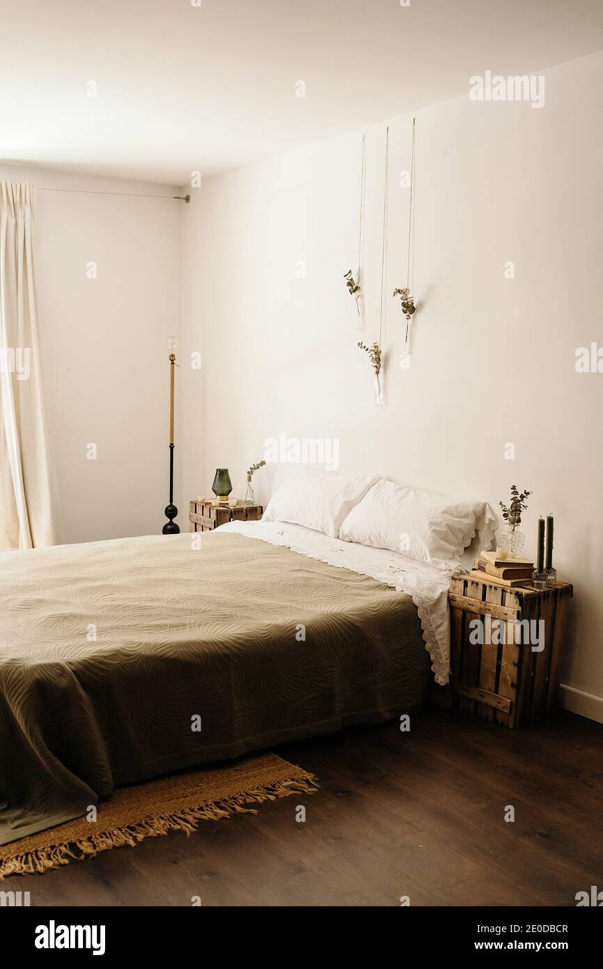Helles Schlafzimmer mit minimalistischer Einrichtung inklusive komfortablem Bett und Holz Möbel mit Boho-Dekoration an weißen Wänden Stockfoto