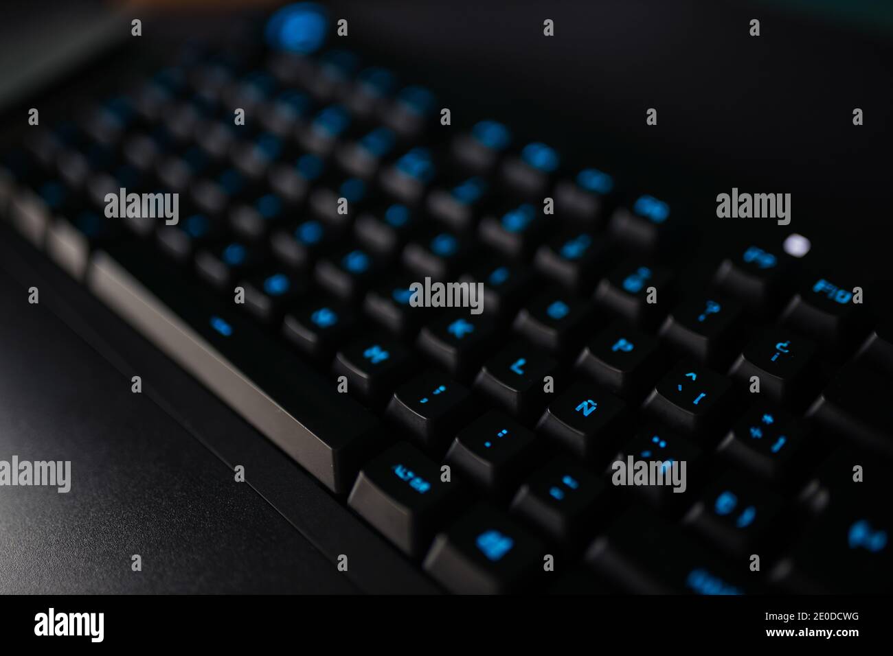 Von oben schwarze Tastatur mit blau beleuchteten Buchstaben platziert Auf dem Schreibtisch in der Nähe des Computermonitors Stockfoto