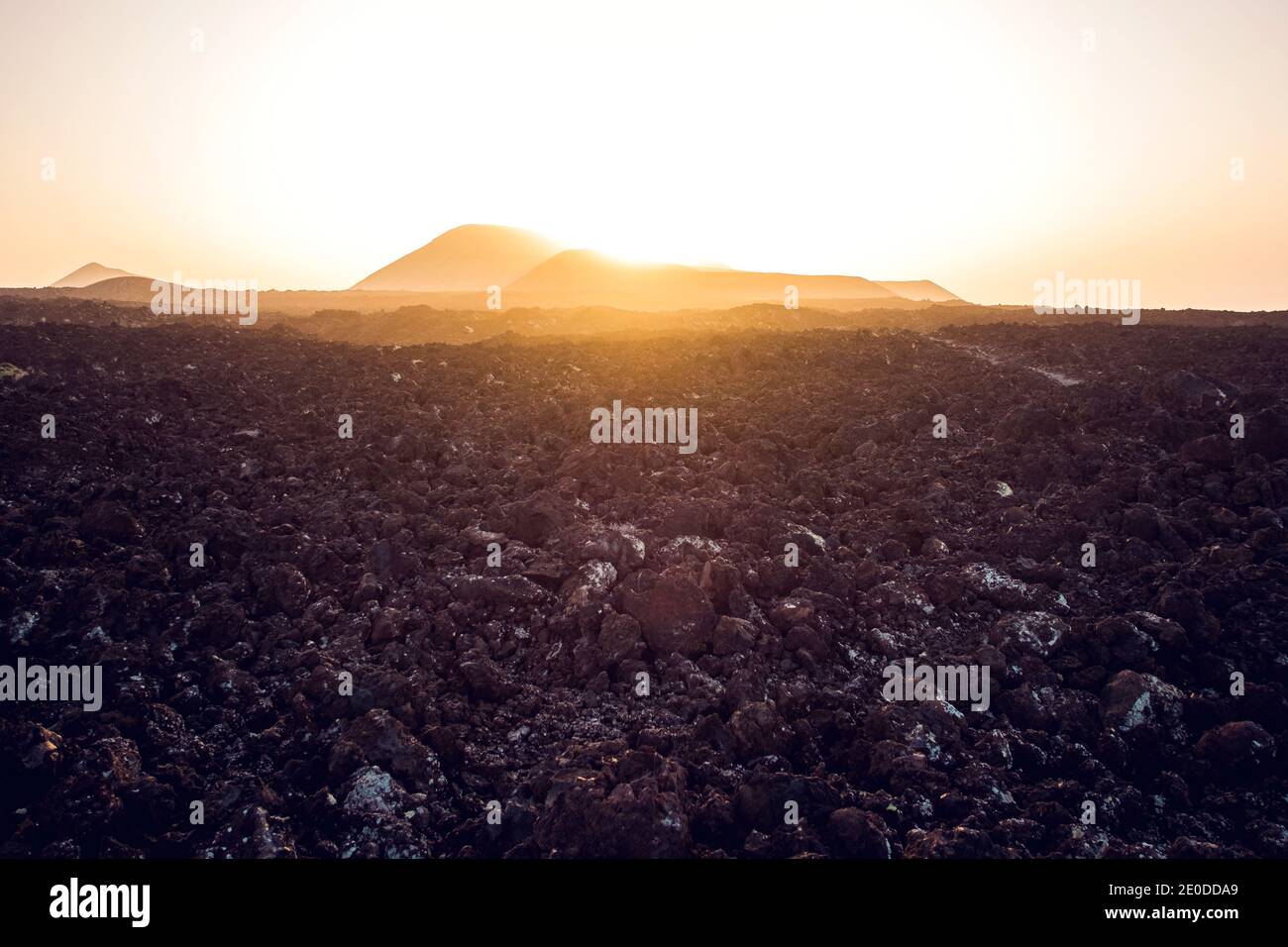 Schmaler grober Pfad in vulkanischem Gelände führt zur Caldera Blanca Und Montana Caldereta Krater gegen wolkenlosen Sonnenuntergang Himmel auf Lanzarote Stockfoto