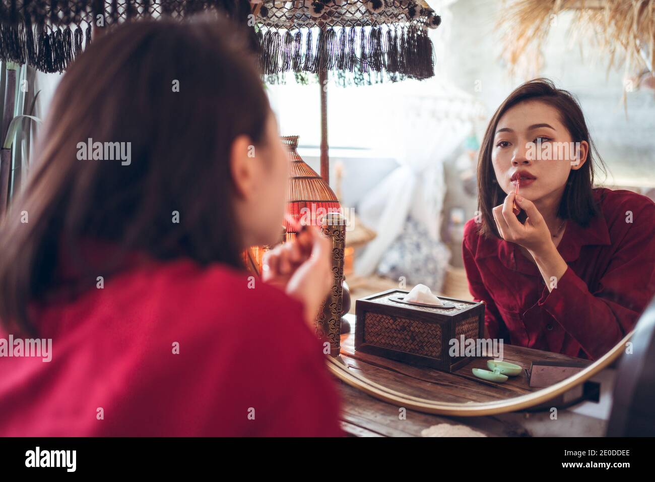 Junge asiatische weibliche Anwendung roten Lippenstift, während im Vordergrund stehen Spiegel im Zimmer mit traditionellem orientalischen Interieur Stockfoto