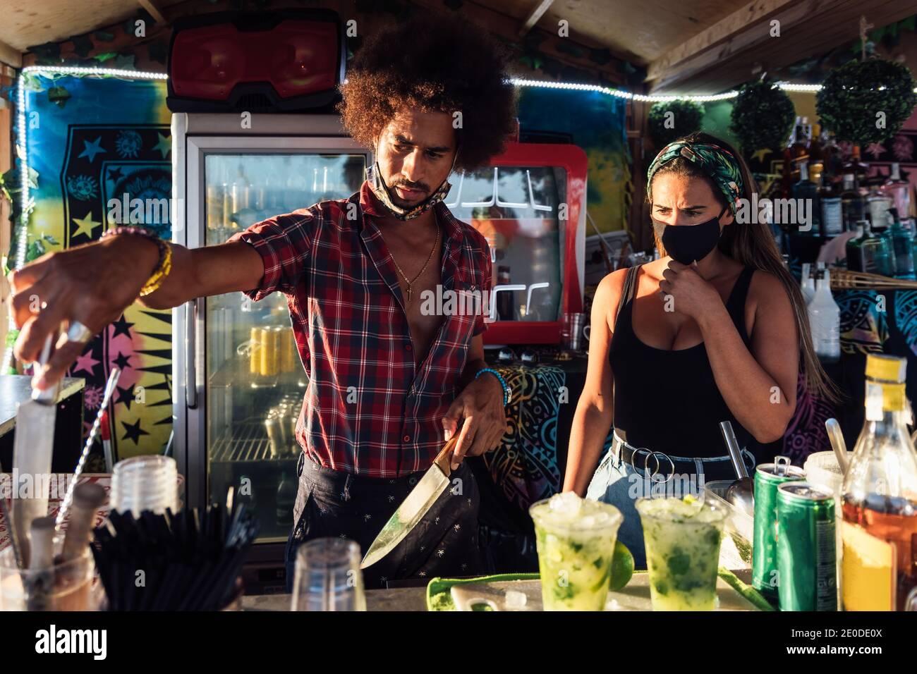 Erwachsene, ethnische Männer und Frauen, die an der Theke stehen und Getränke auf Bestellung zubereiten, während sie in der Außenbar zusammenarbeiten Stockfoto