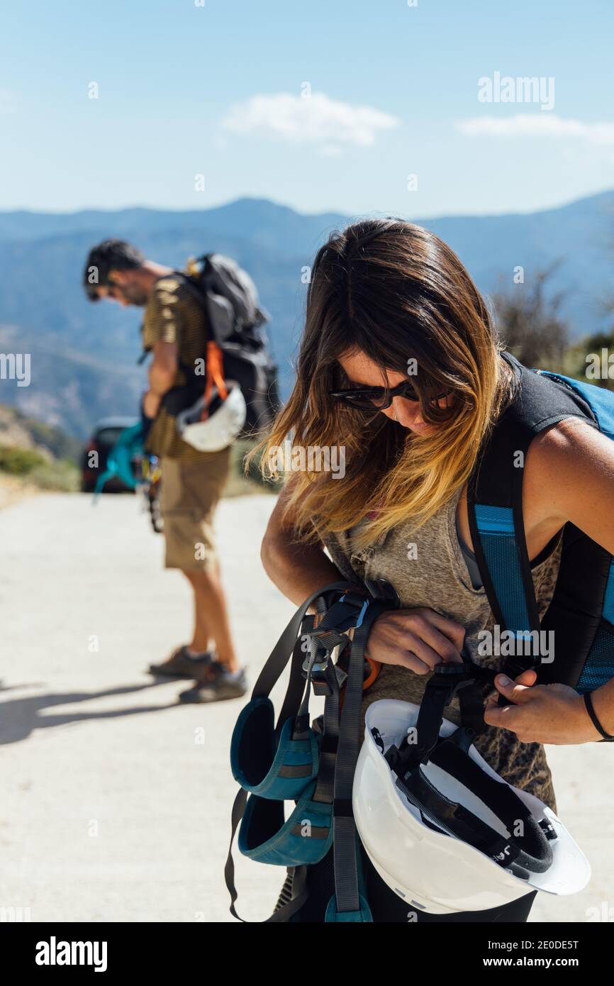 Seitenansicht der Abenteurerin in Aktivbekleidung mit Helm und Ausrüstung zum Abseilen von Befestigungsgurten während der Vorbereitung auf das Training mit Freund in moun Stockfoto