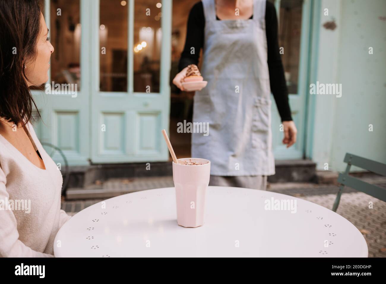Ernte Kellnerin Serving Cupcake zu glücklich weiblichen Kunden sitzen an Tisch mit Glas Frappe Kaffee in gemütlichen Süßwarencafe Stockfoto