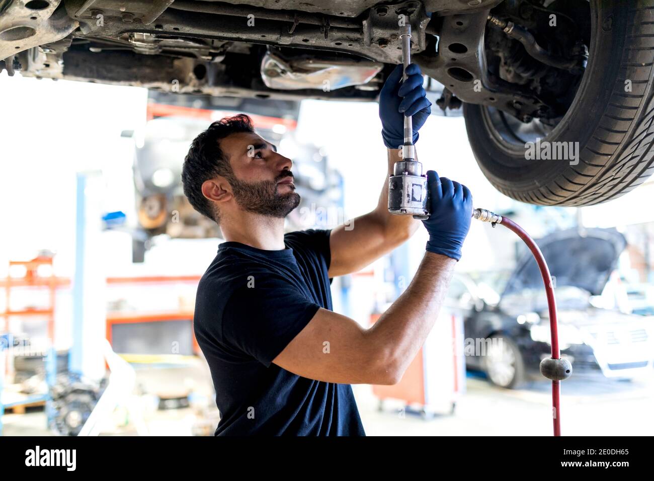 Beschäftigte männliche Techniker mit Spezialinstrument und Befestigung Auto während Arbeiten in modernem Service Stockfoto