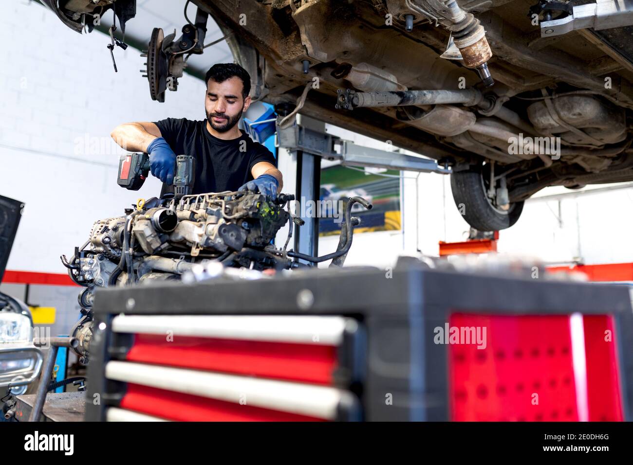 Niedriger Winkel der fokussierten männlichen Mechaniker mit elektrischen Schraubendreher Befestigung Motor des Autos während der Arbeit im Service Stockfoto