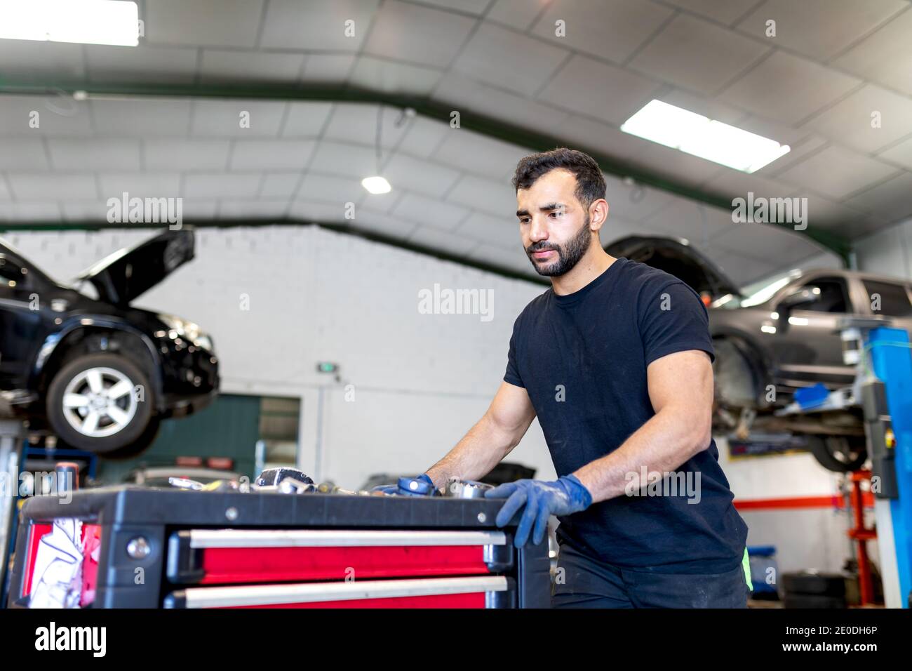 Serious männlichen Techniker in Handschuhen zu Fuß mit Werkzeugschrank in Moderner Autoservice Stockfoto