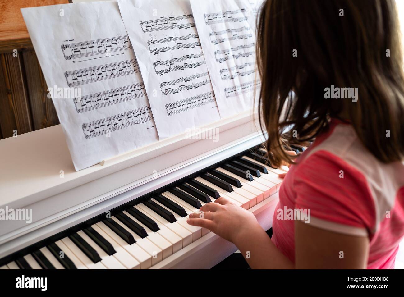 Seitenansicht der positiven kleinen Mädchen in legerer Kleidung lesen Musik und Klavierspiel während der Probe zu Hause Stockfoto