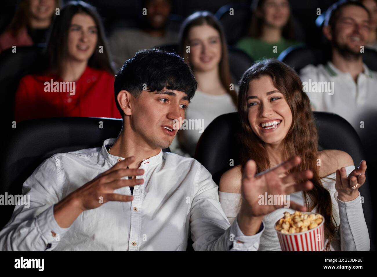 Frontansicht des jungen Mannes, der im Kino lacht, gestikiert und Komödie diskutiert. Selektive Fokus der kaukasischen Mann und atemberaubende Frau genießen schöne lustige Film. Konzept der Unterhaltung. Stockfoto