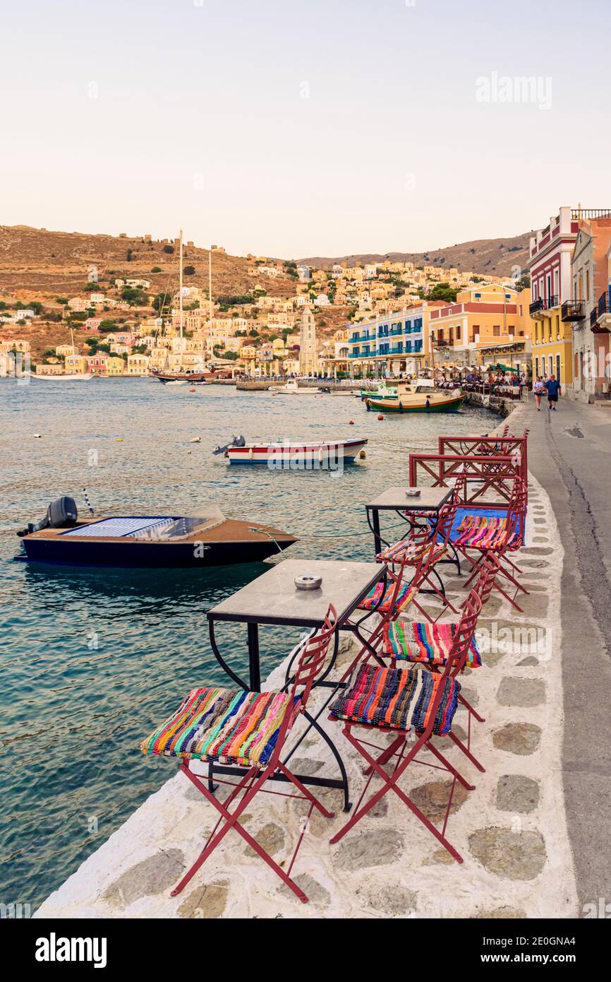 Der szenische Tisch und Stuhl gesäumt Uferpromenade von Yialos Stadt, auf der Insel Symi, Griechenland Stockfoto