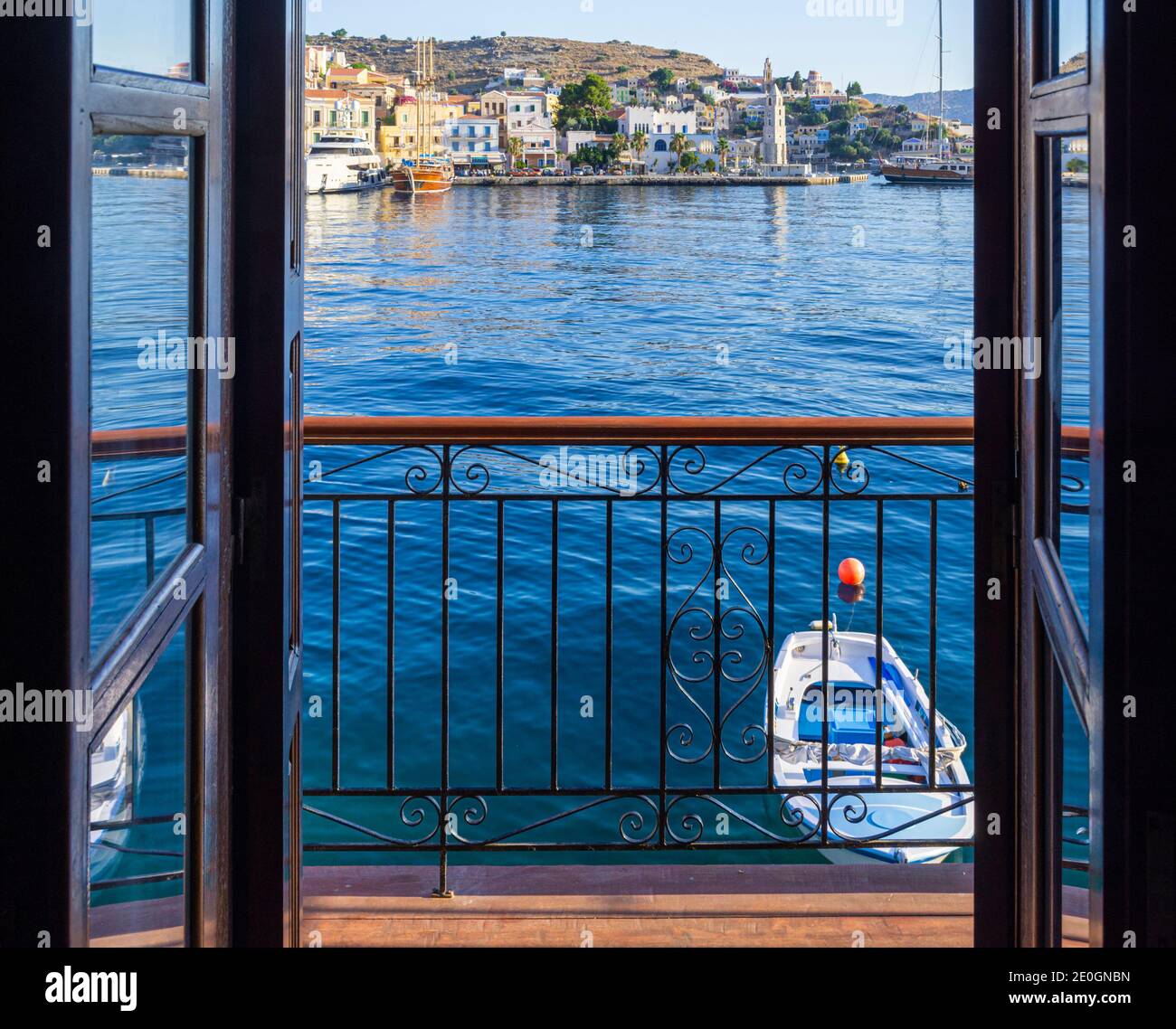 Blick durch eine Tür über einen schmiedeeisernen Balkon und ein kleines Boot zum Hafen von Gialos, Symi Island, Dodekanes, Griechenland Stockfoto