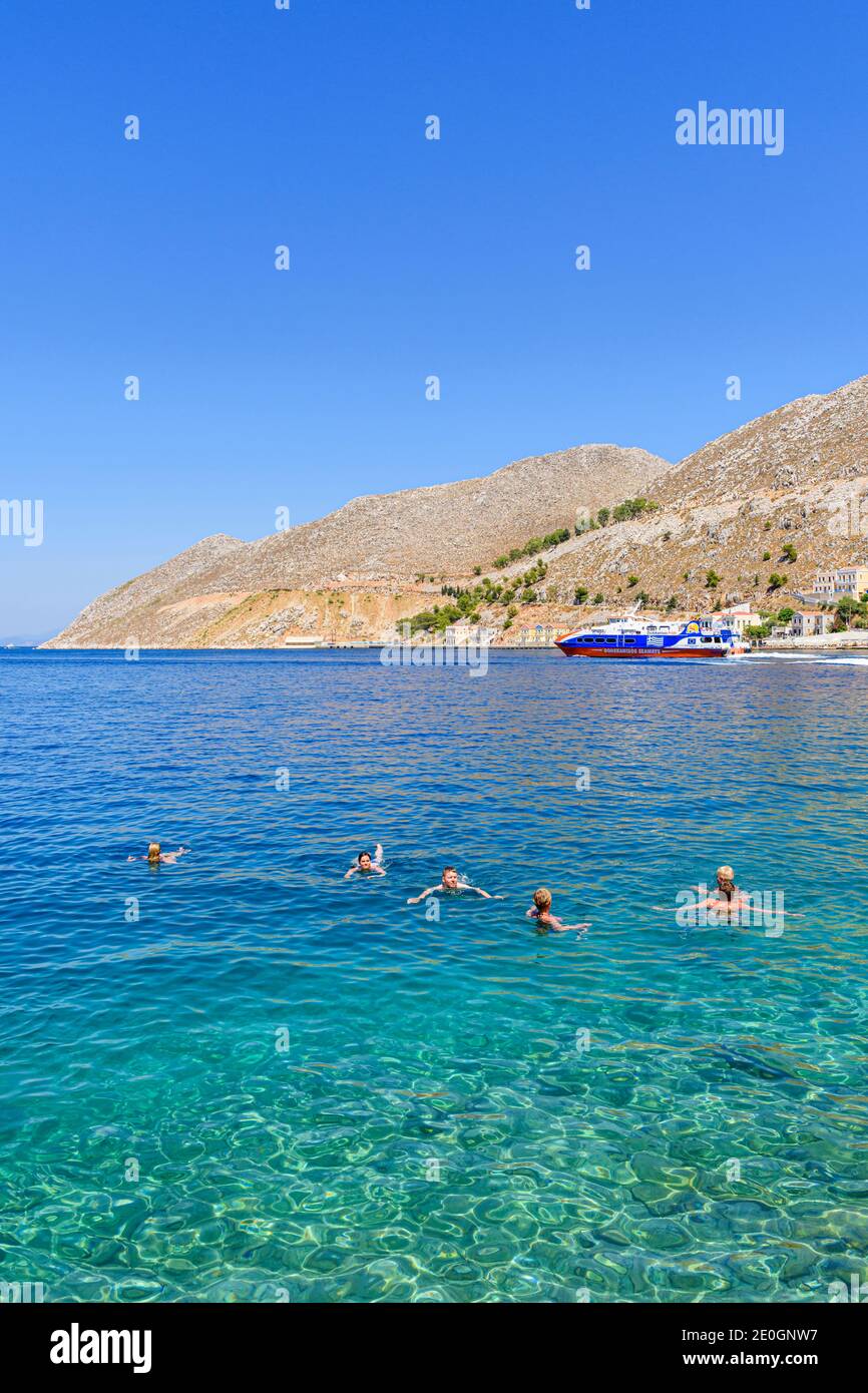 Menschen, die vor der Küste der Stadt Gialos auf der Insel Symi, Dodekanes, Griechenland schwimmen Stockfoto